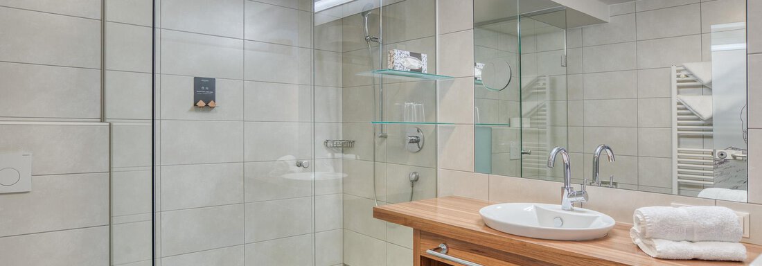 Ein modernes Bad mit Glasduschkabine und Holzwaschtisch. Helle Fliesen und praktische Badaccessoires schaffen eine angenehme Atmosphäre. - Hotel Falknerhof, am Ursprung - Niederthai