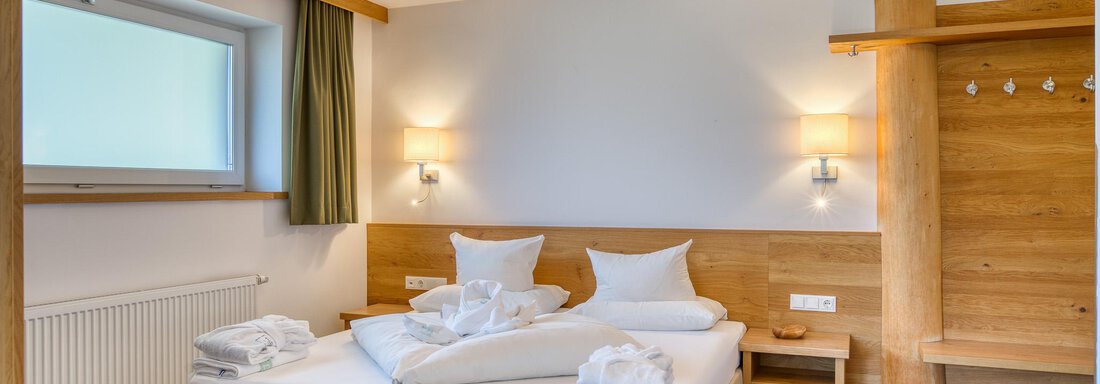 Ein modernes Hotelzimmer mit einem Doppelbett und hellen Holzdetails. Es gibt genügend Tageslicht durch ein Fenster und die Einrichtung ist minimalistisch und gemütlich. - Hotel Falknerhof, am Ursprung - Niederthai