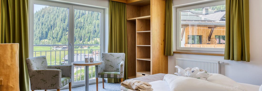Ein gemütliches Zimmer mit einem Doppelbett und einem schönen Ausblick auf die Berge. Es gibt zwei Stühle und einen Tisch, ideal zum Entspannen. - Hotel Falknerhof, am Ursprung - Niederthai