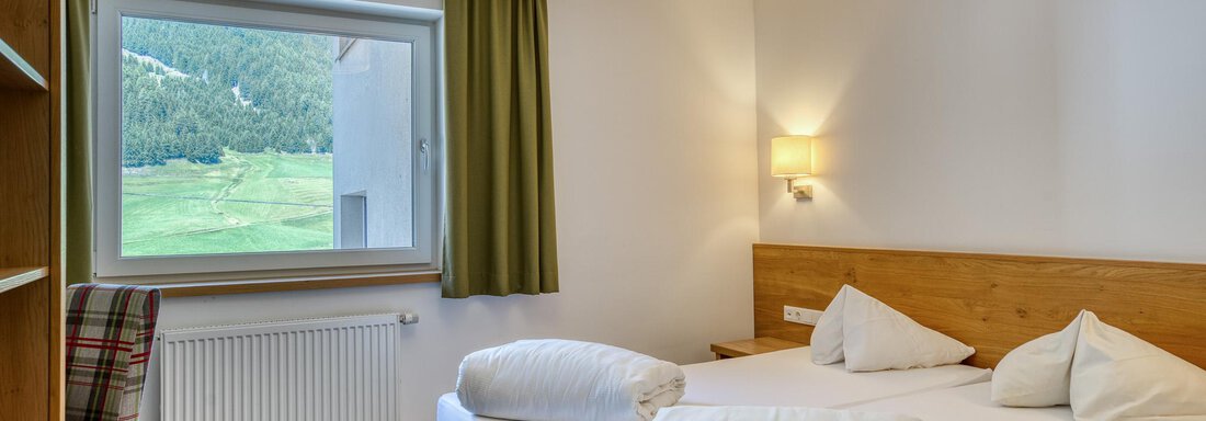 Ein helles Schlafzimmer mit zwei Einzelbetten und einer großen Fensterfront. Der Raum hat einen gemütlichen Stil mit Holzmöbeln und einem Blick auf die grüne Landschaft. - Hotel Falknerhof, am Ursprung - Niederthai