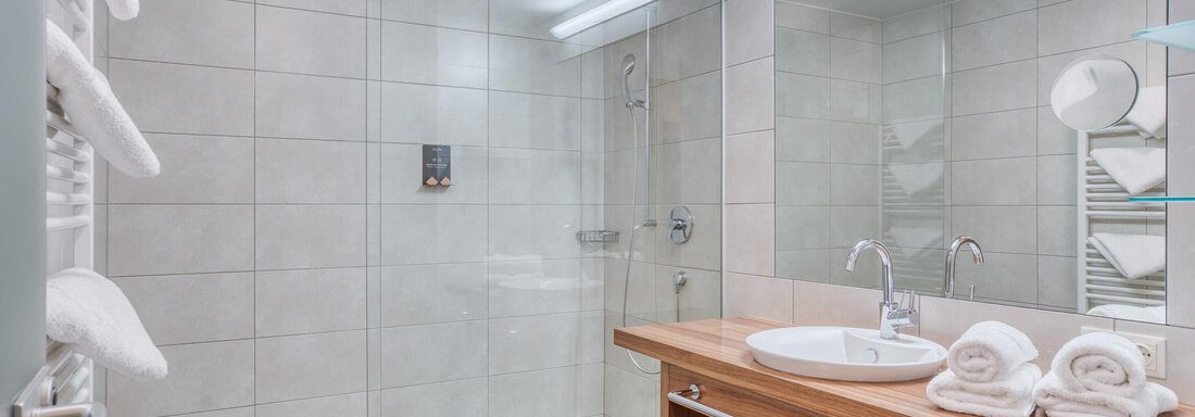 Ein modernes Badezimmer mit einer Glasdusche und einem Holzwaschtisch. Saubere Handtücher liegen ordentlich bereit. - Hotel Falknerhof, am Ursprung - Niederthai