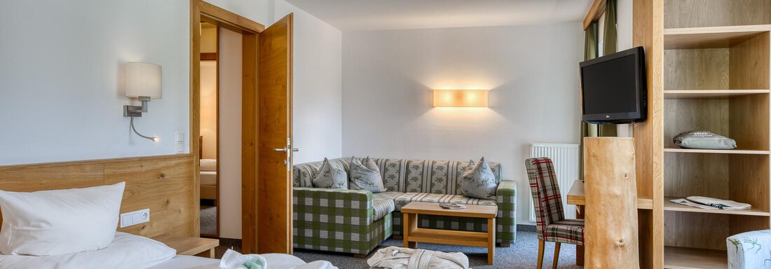 Ein gemütliches Hotelzimmer mit einem Doppelbett und einer Sitzecke. Es gibt einen Fernseher und einen Holzschrank. - Hotel Falknerhof, am Ursprung - Niederthai