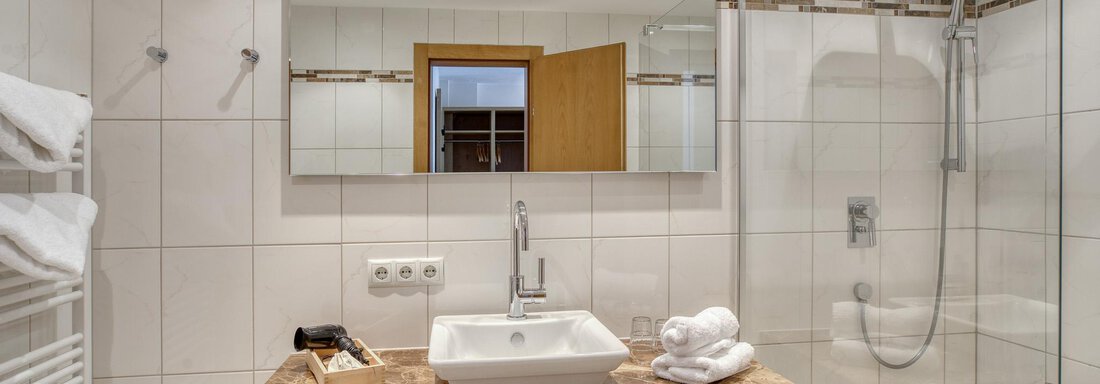 Ein modernes Badezimmer mit einer eleganten Waschbeckenplatte aus Marmor. Es ist hell und sauber, mit einer großen Spiegelwand und einer Duschkabine. - Hotel Falknerhof, am Ursprung - Niederthai