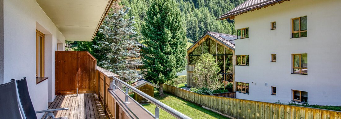 Ein Balkon mit zwei Stühlen, umgeben von grünen Bäumen und Bergen. Im Hintergrund sind zwei Gebäude sichtbar, die einladend wirken. - Hotel Falknerhof, am Ursprung - Niederthai