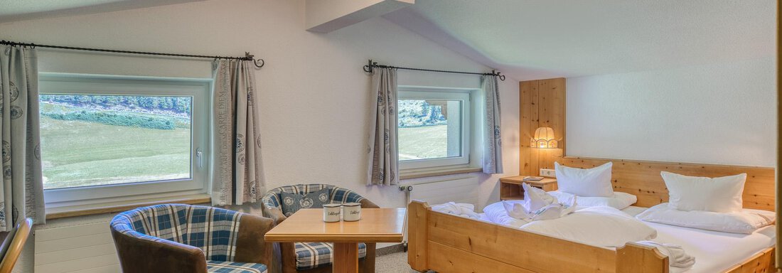 Ein gemütliches Zimmer mit zwei Betten und einem kleinen Tisch. Große Fenster lassen viel Tageslicht herein und bieten einen Blick auf die Landschaft. - Hotel Falknerhof, am Ursprung - Niederthai