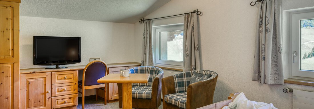 Ein gemütliches Zimmer mit Holzmobiliar und einer Sitzecke. Ein Fernseher und große Fenster sorgen für ein helles Ambiente. - Hotel Falknerhof, am Ursprung - Niederthai