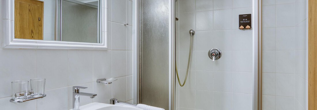 Ein modernes Bad mit einer Dusche, einem Waschbecken und einem Spiegel. Die Wände sind hell gefliest und es gibt weiße Handtücher. - Hotel Falknerhof, am Ursprung - Niederthai