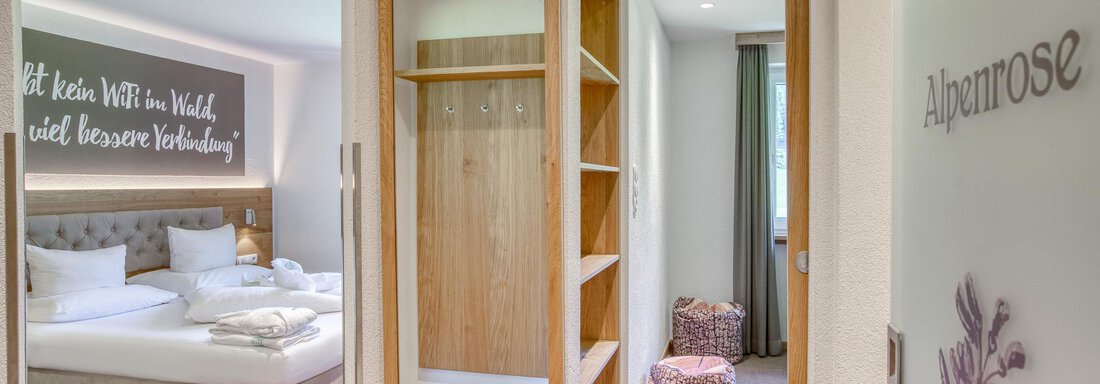 Ein heller Hotelflur mit Zugang zu einem gemütlichen Schlafzimmer. Die Wand ist mit einem inspirierenden Spruch dekoriert, und es gibt einen Holzkleiderschrank. - Hotel Falknerhof, am Ursprung - Niederthai