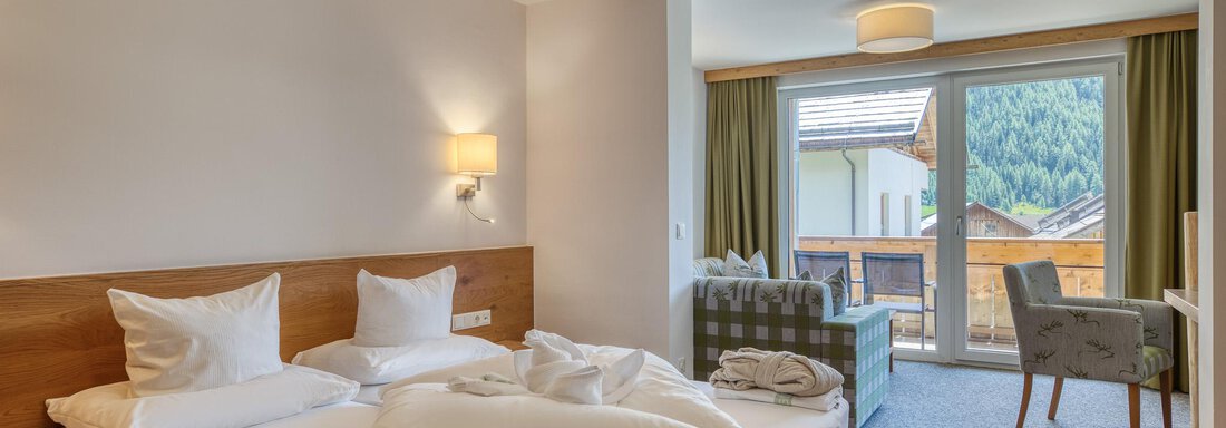 Ein modernes Hotelzimmer mit einem großen Bett und gemütlichen Möbeln. Durch die Fenster blickt man auf eine wunderschöne Berglandschaft. - Hotel Falknerhof, am Ursprung - Niederthai