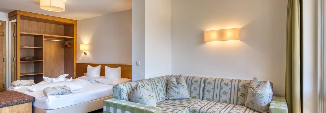 Ein gemütliches Hotelzimmer mit einem Sofa und einem Bett. Die Wände sind hell und es gibt große Fenster mit natürlichem Licht. - Hotel Falknerhof, am Ursprung - Niederthai