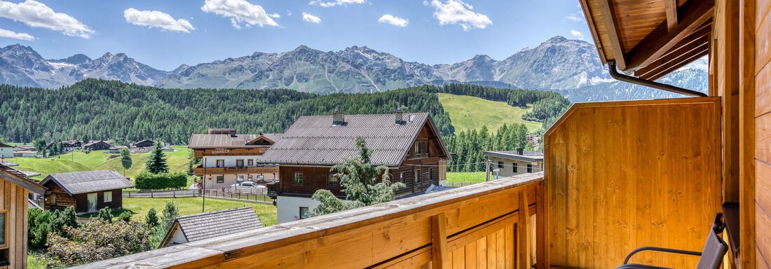 Ein Balkon mit Holzgeländer und zwei Stühlen bietet einen wunderschönen Blick auf die Berge und die grünen Wiesen. Der Himmel ist klar und blau, was die idyllische Atmosphäre unterstreicht. - Hotel Falknerhof, am Ursprung - Niederthai
