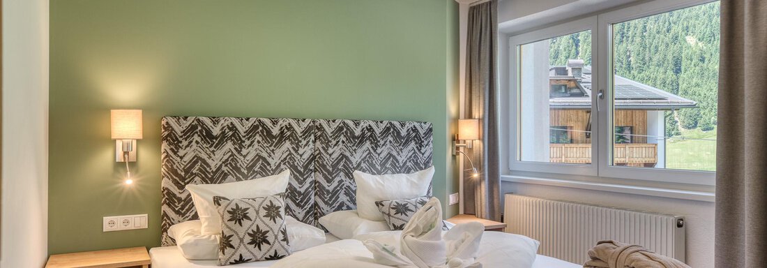 Ein modernes Schlafzimmer mit einem Doppelbett und stilvollen Kissen. Große Fenster bieten einen Blick auf die Natur draußen. - Hotel Falknerhof, am Ursprung - Niederthai