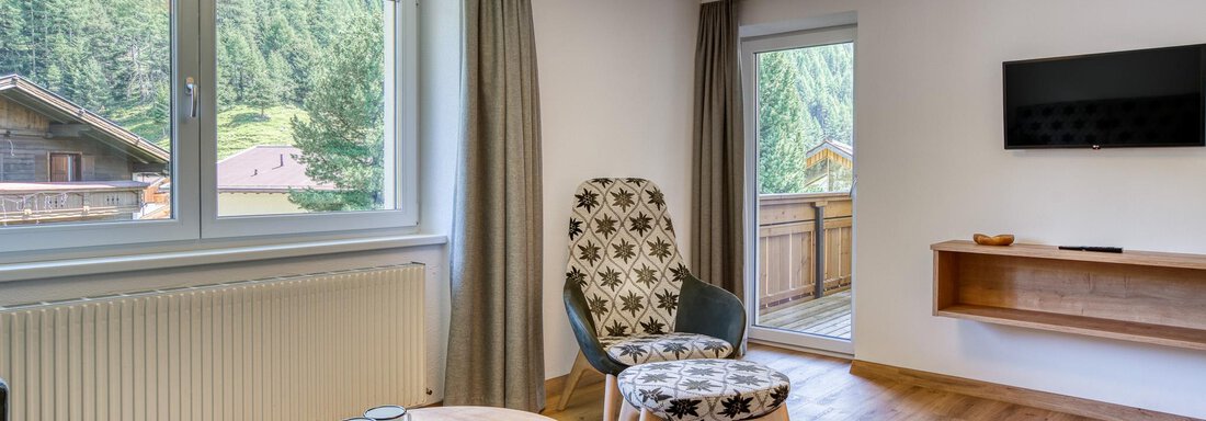 Ein helles Wohnzimmer mit großen Fenstern und Blick auf die Natur. Die Einrichtung ist modern und gemütlich, mit einem runden Tisch und bequemen Stühlen. - Hotel Falknerhof, am Ursprung - Niederthai