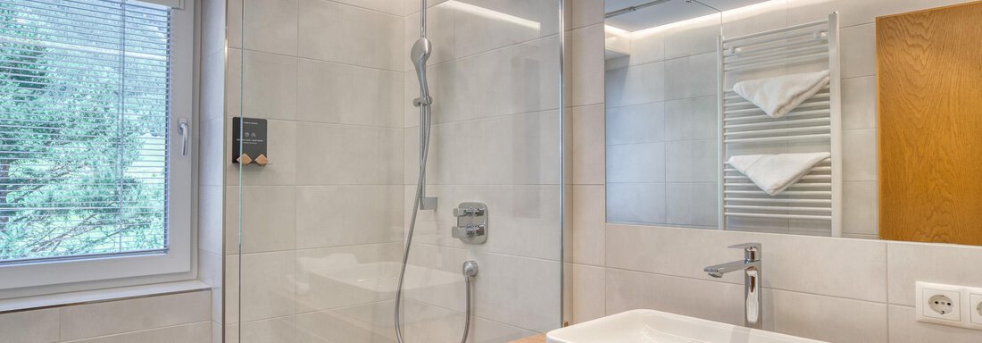 Ein modernes Badezimmer mit einer Glasdusche und einem großen Spiegel. Der Raum ist hell und freundlich, mit einem Waschtisch aus Holz und weißen Handtüchern. - Hotel Falknerhof, am Ursprung - Niederthai