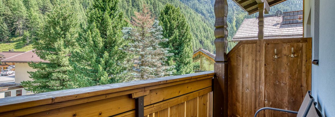 Ein Balkon mit Holzgeländer und zwei Stühlen. Im Hintergrund sind grüne Berge und Bäume zu sehen. - Hotel Falknerhof, am Ursprung - Niederthai