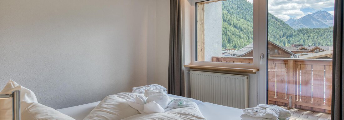 Ein gemütliches Schlafzimmer mit einem großen Bett und frischen Handtüchern. Durch die Fensterblick auf die Berge und einen Balkon. - Hotel Falknerhof, am Ursprung - Niederthai