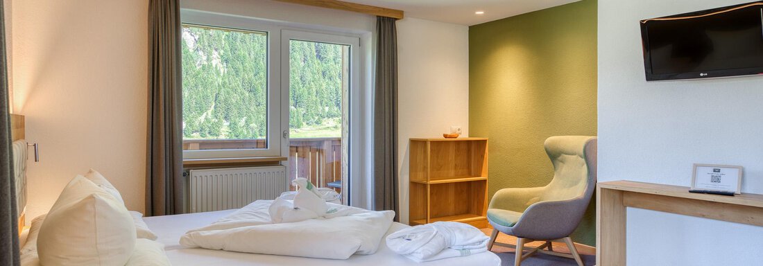 Ein gemütliches Hotelzimmer mit einem großen Bett und einem bequemen Sessel. Die Fenster bieten Blick auf die umliegende Natur. - Hotel Falknerhof, am Ursprung - Niederthai