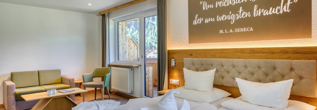Ein modernes Zimmer mit einem Doppelbett und einer gemütlichen Sitzecke. An der Wand befindet sich ein Zitat von Seneca. - Hotel Falknerhof, am Ursprung - Niederthai