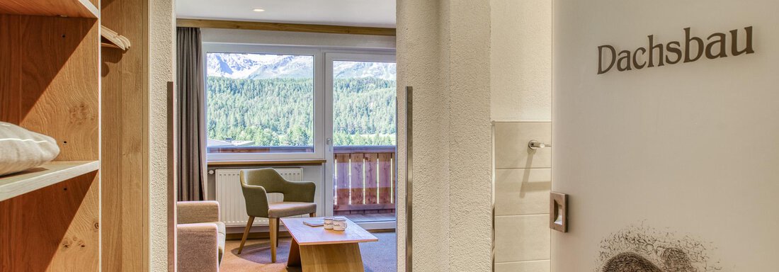 Ein gemütlicher Raum mit einem Holzregal und einer gemütlichen Sitzecke. Durch das große Fenster hat man einen Blick auf die Natur. - Hotel Falknerhof, am Ursprung - Niederthai