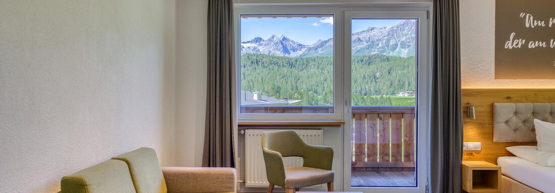 Ein gemütliches Hotelzimmer mit Sitzmöglichkeiten und einem Tisch. Große Fenster bieten einen Blick auf die Berge und die Natur draußen. - Hotel Falknerhof, am Ursprung - Niederthai