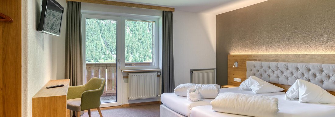 Ein modernes Hotelzimmer mit einem großen Bett, einem Fernseher und einem Balkon. Das Zimmer hat helle Wände und eine gemütliche Sitzgelegenheit. - Hotel Falknerhof, am Ursprung - Niederthai