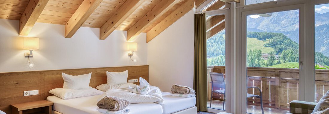 Ein gemütliches Zimmer mit zwei Betten und Holzdecken. Große Fenster bieten einen Blick auf die Berge und den Balkon. - Hotel Falknerhof, am Ursprung - Niederthai