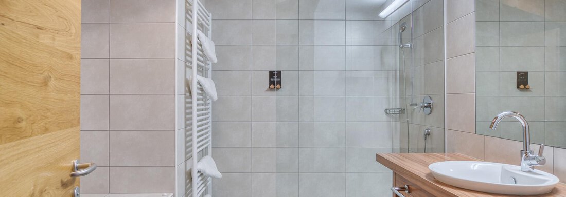 Ein modernes Badezimmer mit Holz- und Fliesenakzenten. Es verfügt über eine Badewanne, eine Dusche und ein elegantes Waschbecken. - Hotel Falknerhof, am Ursprung - Niederthai