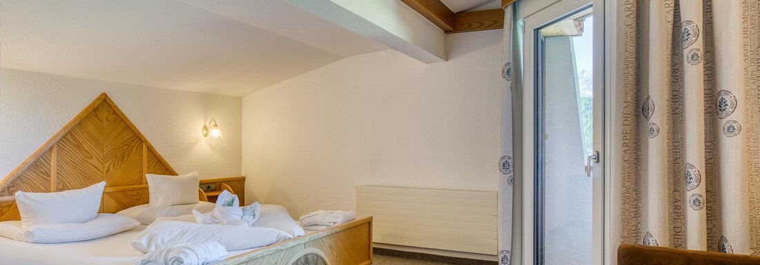 Ein gemütliches Hotelzimmer mit einem großen Bett und frischen Handtüchern. Ein kleiner Tisch und ein Sessel ergänzen die Einrichtung, und es gibt einen Zugang zu einem Balkon. - Hotel Falknerhof, am Ursprung - Niederthai