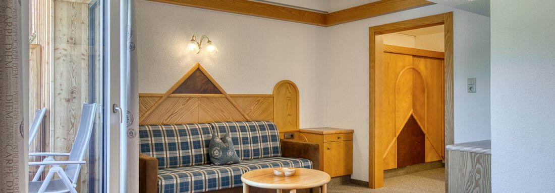 Ein gemütliches Hotelzimmer mit einem Sofa, einem Tisch und einer Tür zur Veranda. Die Holzdetails verleihen dem Raum eine warme Atmosphäre. - Hotel Falknerhof, am Ursprung - Niederthai