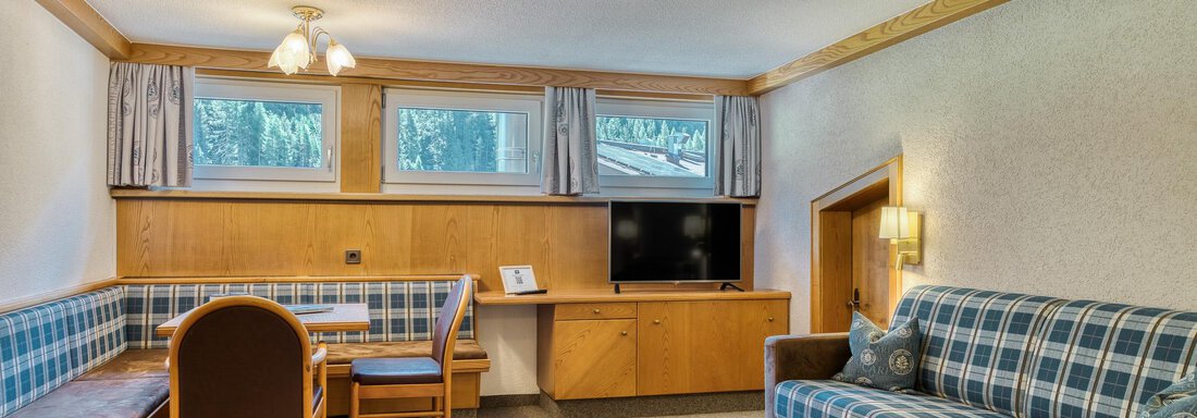 Ein gemütlicher Wohnbereich mit einer Couch und einem Esstisch. Die großen Fenster lassen viel Licht herein und bieten einen Blick nach draußen. - Hotel Falknerhof, am Ursprung - Niederthai