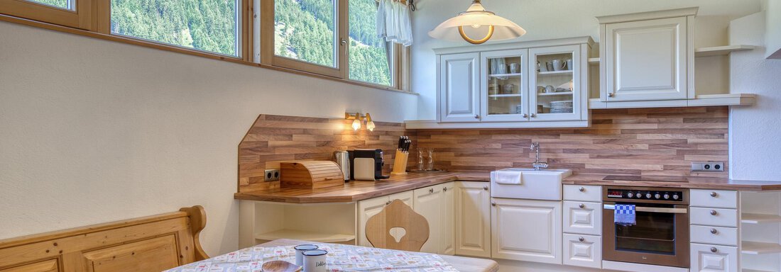 Eine helle Küche mit Holzverkleidung und großen Fenstern. Der Tisch ist mit einem Tischdecken dekoriert und es gibt moderne Küchengeräte. - Hotel Falknerhof, am Ursprung - Niederthai