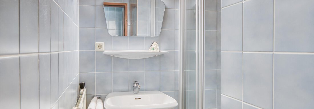 Ein kleines Badezimmer mit blauen Fliesen und einer Dusche. Es enthält ein Waschbecken und einen Spiegel. - Hotel Falknerhof, am Ursprung - Niederthai