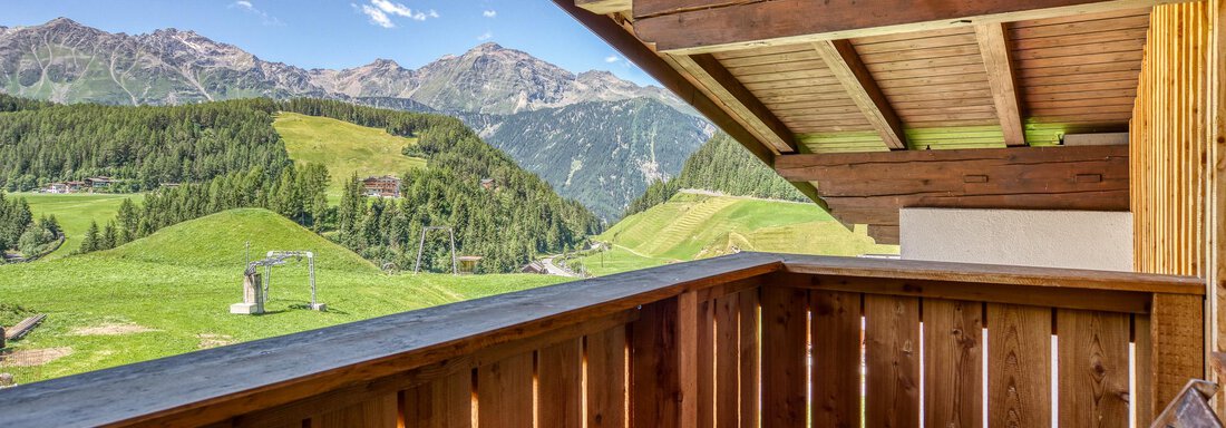 Ein Balkon mit Holzgeländer und Blick auf grüne Hügel und Berge. Der Himmel ist klar und sonnig. - Hotel Falknerhof, am Ursprung - Niederthai