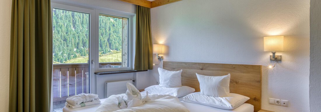 Ein gemütliches Zimmer mit zwei Betten und sanften Farben. Durch das Fenster ist eine grüne Berglandschaft sichtbar. - Hotel Falknerhof, am Ursprung - Niederthai