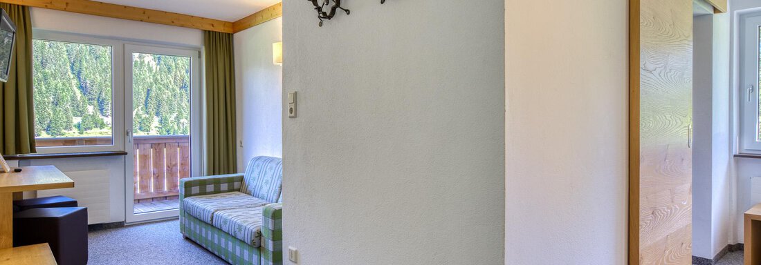 Ein heller Raum mit einem gemütlichen Sofa und einem Schreibtisch. Große Fenster bieten einen Blick nach draußen und lassen viel Tageslicht herein. - Hotel Falknerhof, am Ursprung - Niederthai