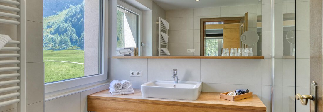Ein modernes Badezimmer mit Holzregal und großen Fenstern. Die Aussicht zeigt eine grüne Landschaft und bietet viel Tageslicht. - Hotel Falknerhof, am Ursprung - Niederthai
