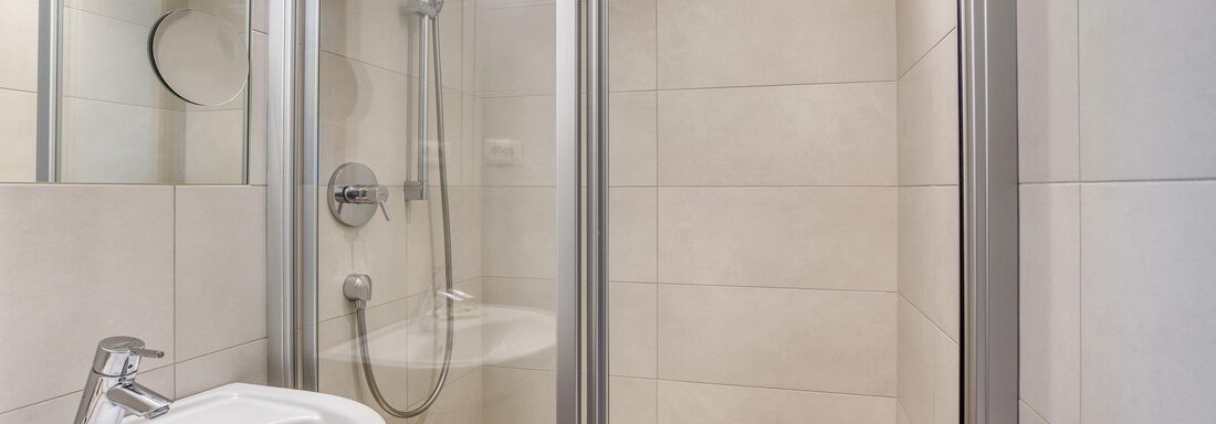 Ein modernes Badezimmer mit einer Duschkabine und einem Waschbecken. Die Wände sind hell gefliest und die Ausstattung ist funktional. - Hotel Falknerhof, am Ursprung - Niederthai