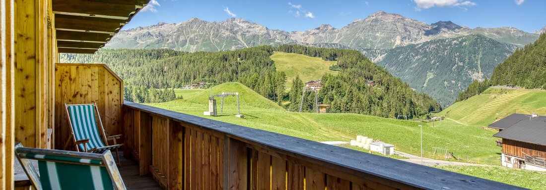 Ein schöner Balkon mit Holzgeländer und Liegestühlen. Im Hintergrund erstreckt sich eine malerische Berglandschaft mit grünen Hügeln und blauem Himmel. - Hotel Falknerhof, am Ursprung - Niederthai