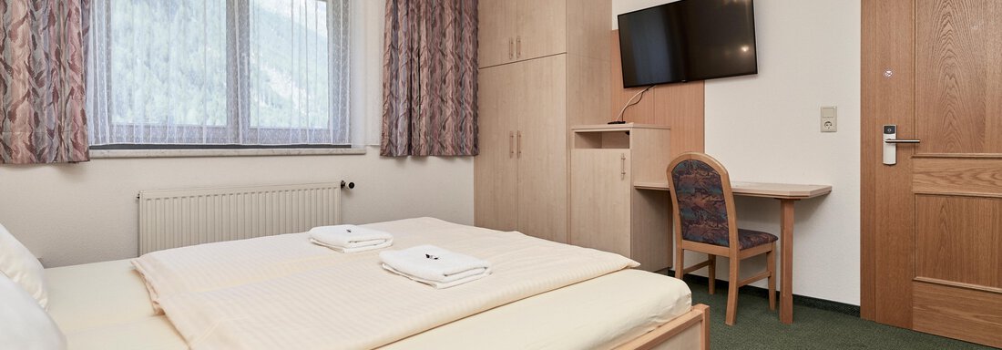 A cozy bedroom with a double bed and two towels. The room is bright and stylishly furnished, with a desk and a television. - Hotel Tauferberg - Niederthai