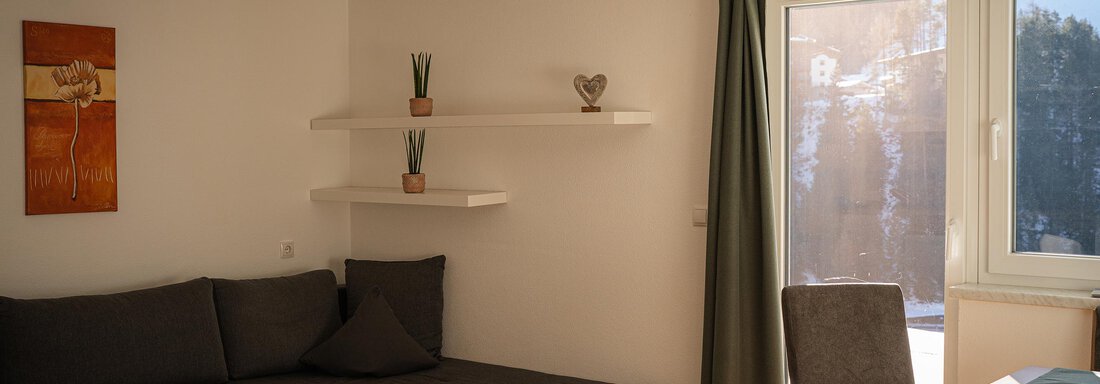 Ein modernes Wohnzimmer mit einem gemütlichen Sofa und einem kleinen Tisch. Große Fenster lassen viel Licht herein und bieten Ausblick auf die Umgebung. - Sonnenhof - Niederthai