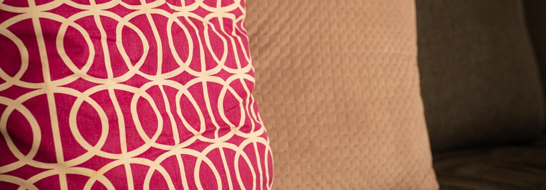 Ein gemütliches Sofa mit zwei Kissen. Eines ist pink mit einem grafischen Muster, das andere ist beige und hat eine strukturierten Oberfläche. - Sonnenhof - Niederthai
