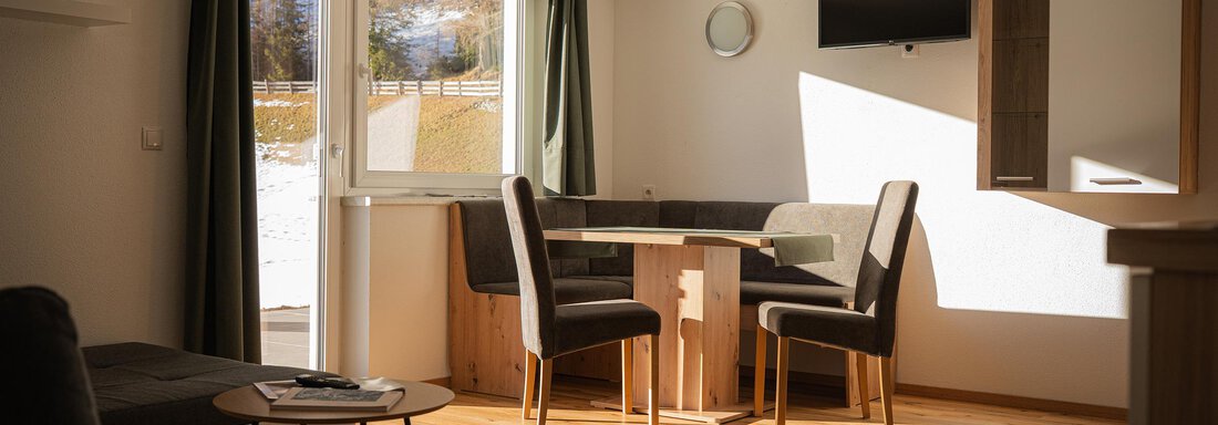 Ein modernes Wohnzimmer mit einem Esstisch und Stühlen. Die großen Fenster lassen viel Tageslicht hinein. - Sonnenhof - Niederthai
