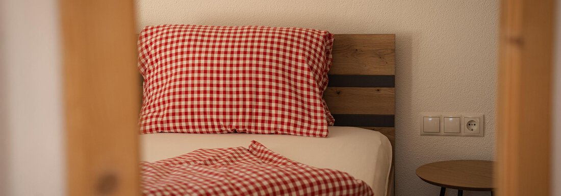 Ein gemütliches Schlafzimmer mit einem Bett und karierten Kissen. Neben dem Bett steht ein kleiner Nachttisch. - Sonnenhof - Niederthai