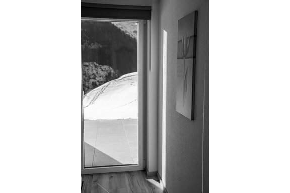 Ein moderner Raum mit einem großen Fenster, das einen Blick auf schneebedeckte Landschaften bietet. An der Wand hängt ein minimalistisches Gemälde. - Sonnenhof - Niederthai