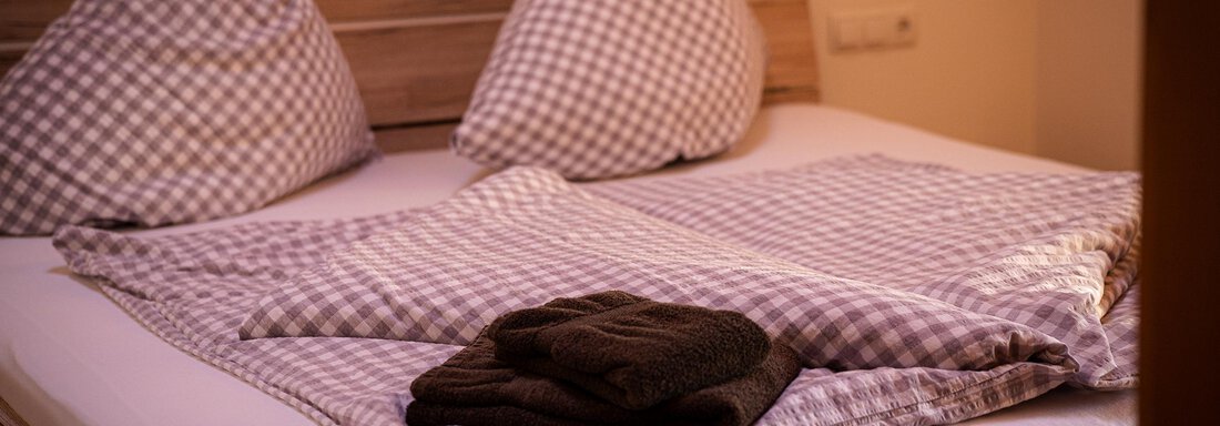 Ein gemütliches Schlafzimmer mit einem Doppelbett und karierten Kissen. Eine Decke und ein Handtuch liegen ordentlich auf der Bettdecke. - Sonnenhof - Niederthai