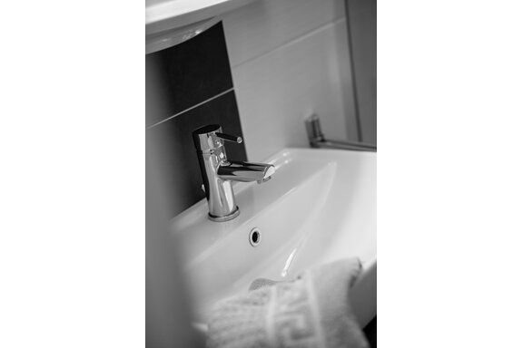 Ein moderner Wasserhahn über einem weißen Waschbecken. Im Hintergrund ist ein Handtuch und eine dunkle Wand sichtbar. - Sonnenhof - Niederthai
