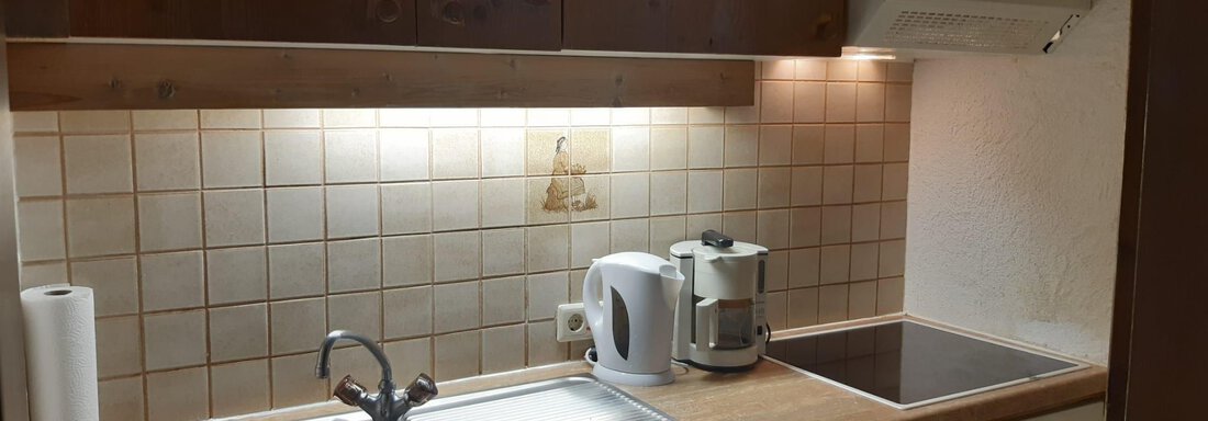 Eine moderne Küche mit Holzregalen, einem Waschbecken und einem Kochfeld. Auf der Arbeitsfläche stehen ein Wasserkocher und eine Kaffeemaschine. - Tirolerhof - Niederthai