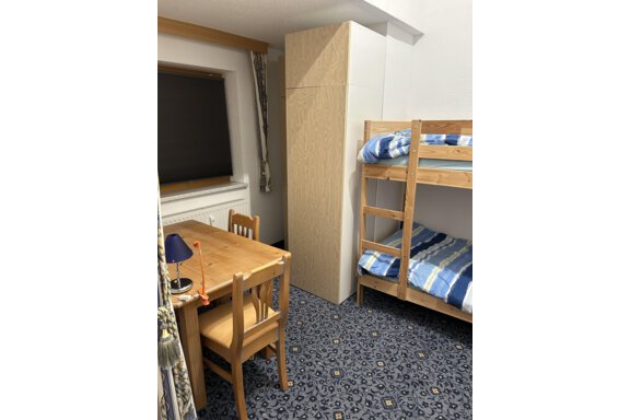A simple bedroom with a bunk bed and a table. The walls are light and the floor is adorned with a carpet-like pattern. - App. Diamant Obergurgl - Obergurgl 