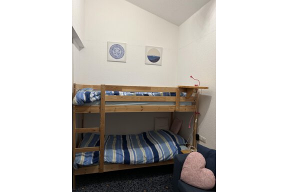 A cozy room with a bunk bed and striped bedcovers. Decorative pictures hang on the wall, and a blue armchair with a heart-shaped cushion stands beside it. - App. Diamant Obergurgl - Obergurgl 
