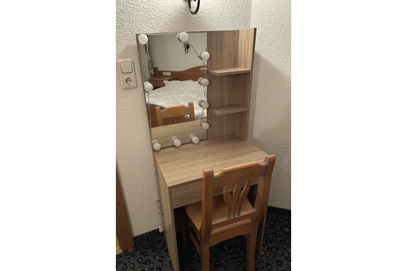 A simple wooden vanity with a mirror and lighting. Next to it is a chair, and in the background, a bed can be seen. - App. Diamant Obergurgl - Obergurgl 